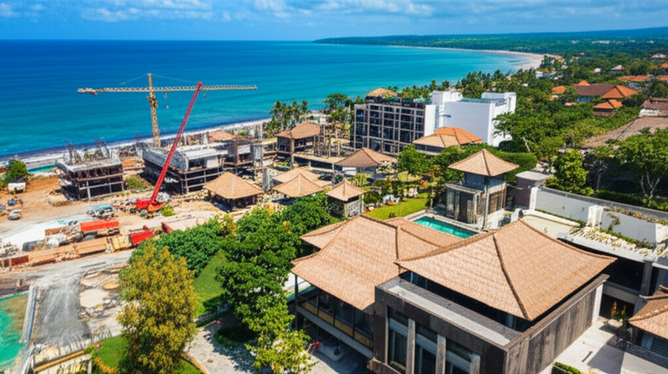 Aerial view of Bali's coastline showing a mix of construction projects, including luxury villas, resorts, and commercial spaces, set against a backdrop of lush green landscapes and the turquoise ocean.