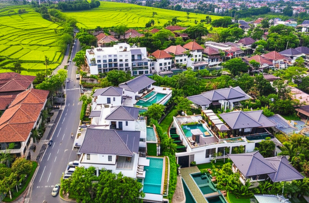 A panoramic view of Bali showcasing modern buildings like resorts, villas, and commercial spaces, set against a backdrop of lush rice paddies and traditional Balinese culture, symbolizing the intersection of progress and preservation.