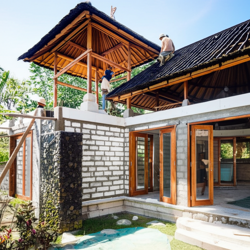 Illustration showing various stages of Balinese villa construction, including wall building, roofing, and window installation with natural materials.