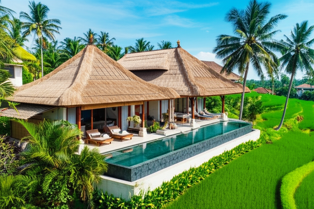 Modern Balinese villa integrated into its tropical surroundings, with a thatch roof and infinity pool overlooking rice paddies.