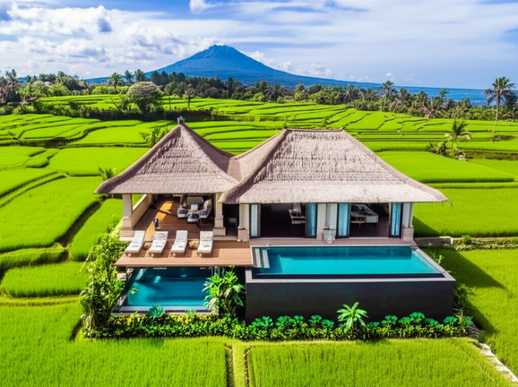 Aerial view of a luxurious Balinese villa surrounded by rice paddies and volcanic mountains, showcasing the blend of modern comfort with traditional Balinese architecture.