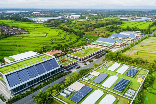 An aerial view of a sustainable industrial park in Bali, showing eco-friendly buildings amidst rice paddies and tropical vegetation, representing responsible industrial development.